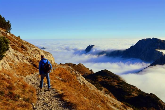 kalnuotas kraštovaizdis, žmogus, vaikščiojantis mažu zigzago taku kalne, turistas, įveikęs debesų lygį