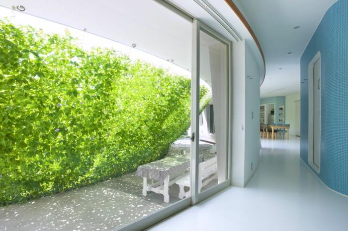 yeşil ekran şeklinde şeffaf teller üzerinde dikey bahçe, beyaz tezgah ve kareli kapaklı beyaz dikdörtgen masa ile bir veranda dinlenme köşesi için bir gölge görevi gören dikey kültür