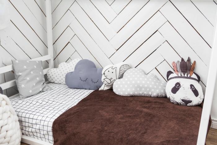 kabinska postelja montessori v kotu sobe montessori, kabinska postelja iz belega lesa, blazine v različnih oblikah, stene pokrite z belim lesom vdolbljene kot parket