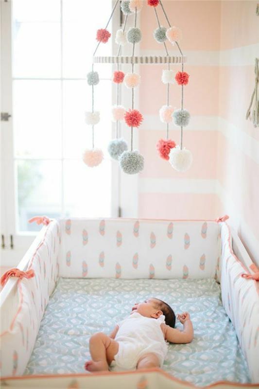 rožinis ir pilkas miegamasis, mergaitės miegamojo apdaila, čiužinys, padengtas pastelinės spalvos paklode, virš lovos kabančios įvairiaspalvės pompomos, lašiša ir baltos sienos