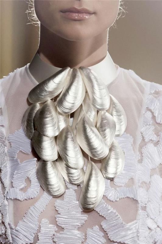 polprosojna bela bluza s čipkastimi okraski in z ogrlico s školjkami srebrne barve, elegantna in šokantna obleka