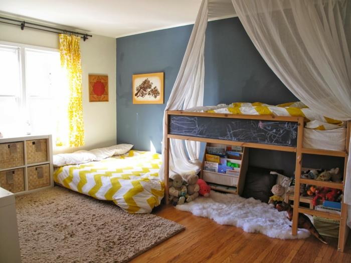 postelja montessori, jaslice brez palic, postelja iz koče montessori, svetla otroška in otroška soba, velika stena v račji modri barvi, rumene zavese z belimi arabeskami, hipoalergenska plišasta rjava preproga