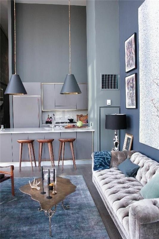 odtenek modre dnevne sobe s kremno belim kavčem in stenami ter preprogo v sivo modri barvi z dolgimi visečimi lučmi v isti barvi