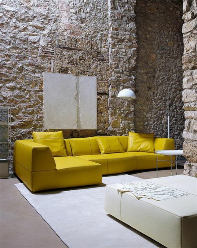 1 svetainė su geltona sofa ir atvira akmens siena, smėlio spalvos kilimas ir svetainė-lempa su geltona sofa