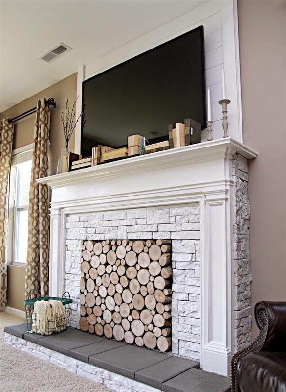dirbtinis dekoratyvinis židinys iš baltų akmenų kaip televizoriaus stovas ir židinys, pripildytas medinių rąstų