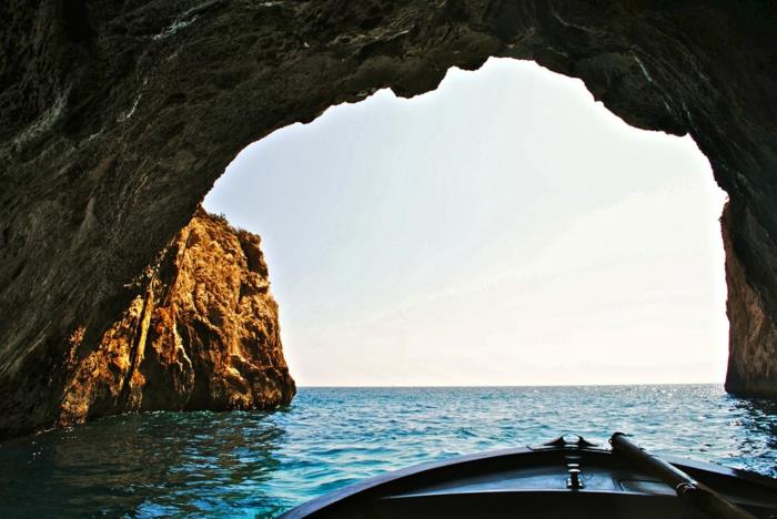 išėjimas iš olos su maža žvejų valtele, be debesų dangus, mėlyni vandenys Grotta azzurra, rudos ir pilkos uolos