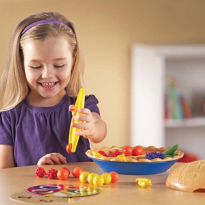 Montessori malzemesi ile 3 yaşında aktivite çocuğu plastik meyveler taklit hamurlu bir tabakta saklamak için, meyveli tart