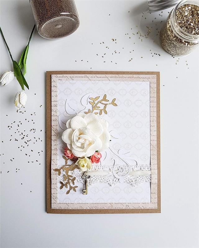 „pasidaryk pats“ gimtadienio atvirukas iš smėlio spalvos popieriaus su knygos puslapio raidžių imitacijomis, rankų darbo atvirukas su balta gėle ir metaline raktų figūrėle