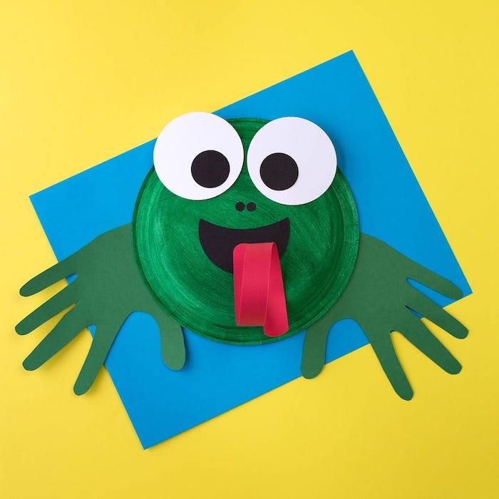 manuel aktivite 4 yaşında yeşil kağıt tabakta bir kurbağa ve yeşil el izleri, kağıttan yapılmış yüz özellikleri