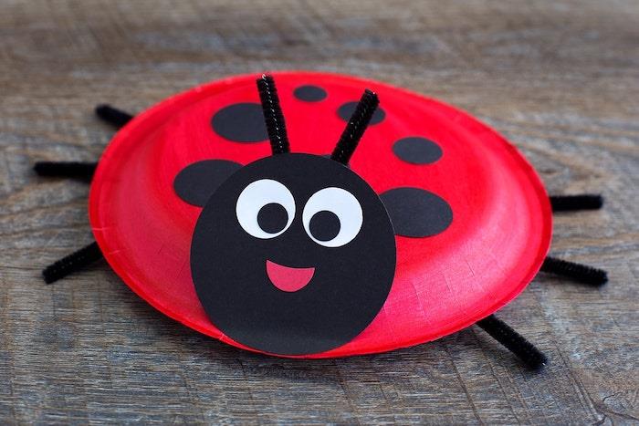 perdirbimo idėja apie vienkartinę raudoną popierinę lėkštę, papuoštą juodais taškeliais ir juodos spalvos apskritimo galvutės lapelio modeliu su antenomis ir vamzdžių valymo kojelėmis, pavasarinė rankinė veikla