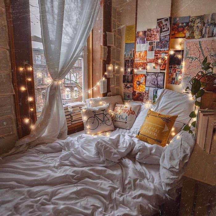 svajonių miegamojo apdaila su jaukia lova, perkrauta pagalvėlėmis, nuotraukų ir knygų puslapių sienų apdaila, interjero šviesos girlianda