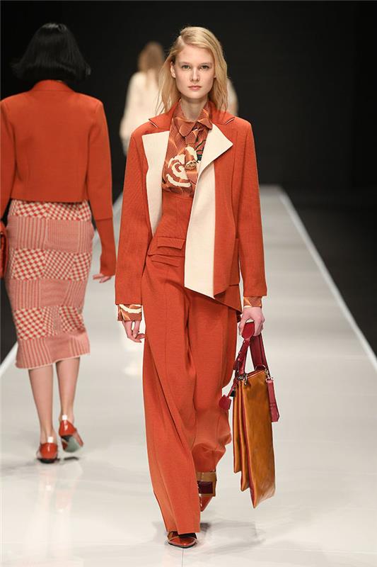 manekenka, ki hodi po vzletno -pristajalni stezi, trenutni modni trendi, oblečena v vse oranžne obleke, sestavljene iz hlače bluze in blazerja