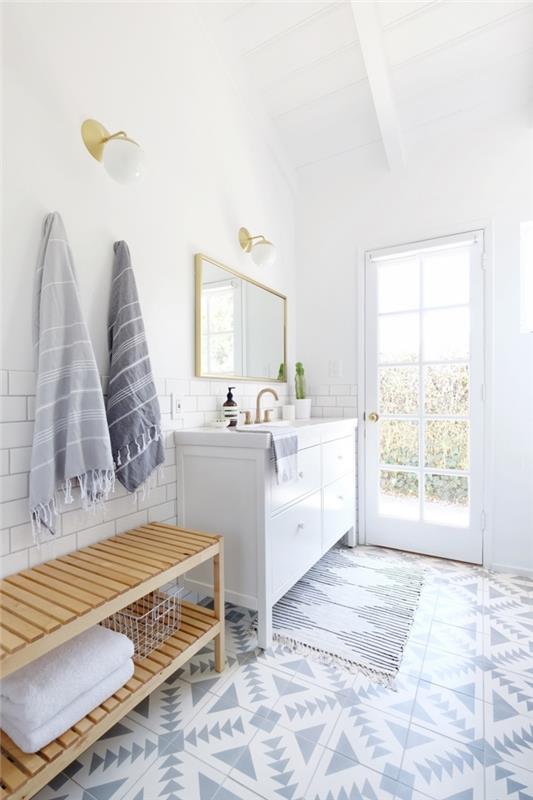 baltos ir šviesiai pilkos spalvos vonios kambarys su žalvario akcentais, dvelkiantis ramybe, balta vonios spintelė