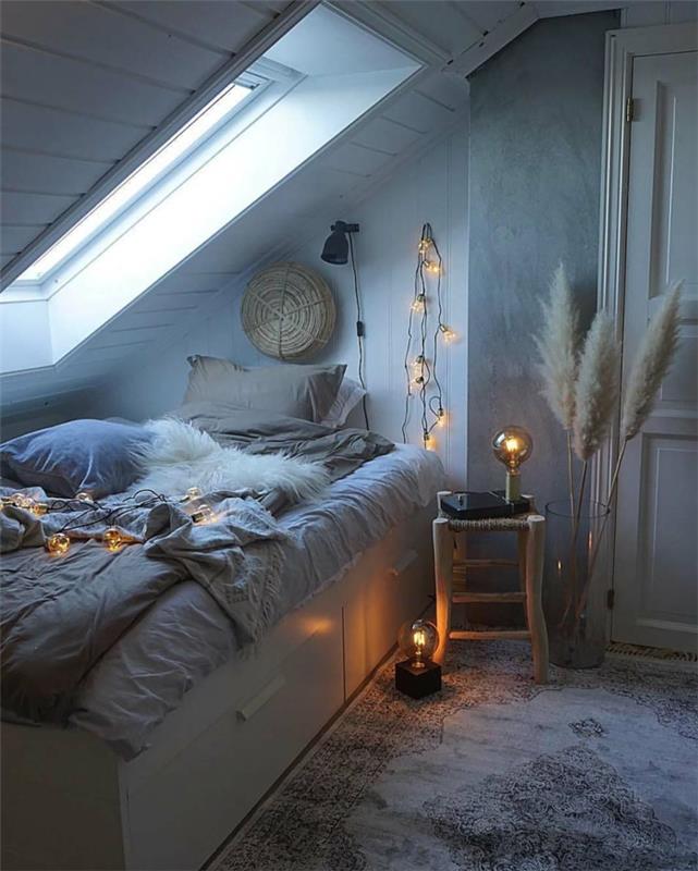 jaukus miegamasis, jaukia atmosfera, svetinga pilka lova, šviesi girlianda, nuožulnus langas, didelė vaza su džiovintomis gėlėmis
