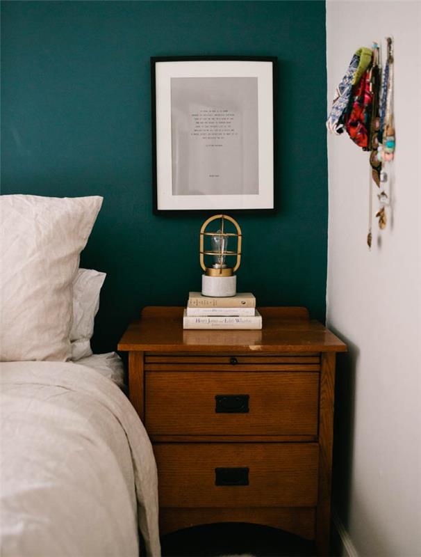 benzininis mėlynas miegamojo dekoras galinei sienai, kaimiškas medinis naktinis stalas, balta patalynė, krūva knygų, originali retro naktinė lempa