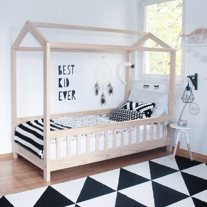 medinė Montessori lova skandinaviškame vaikų kambaryje juoda ir balta, miegamasis su parketu, juodai baltas kilimas su trikampiais