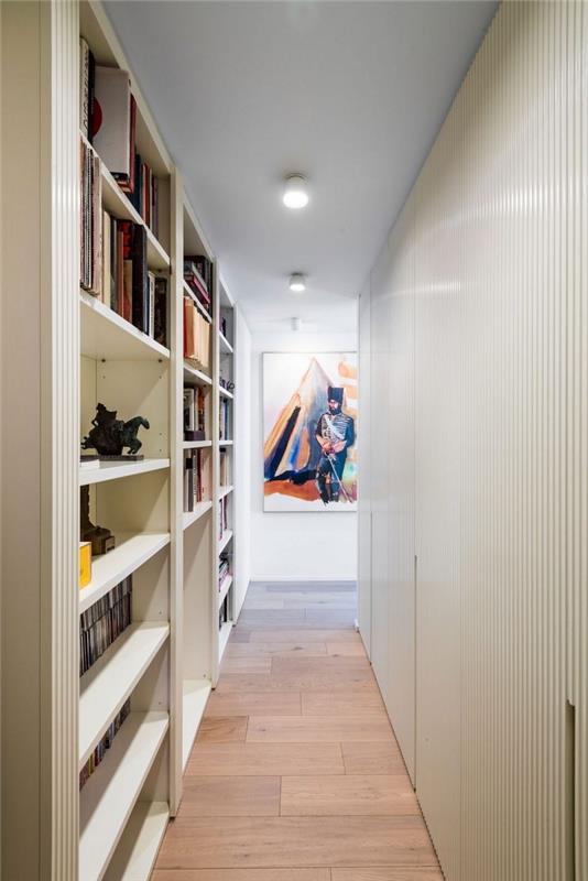 dekoracija dolg in ozek hodnik s knjižnico, razporejeno vzdolž stene, ureditev funkcionalnega ozkega hodnika, stena hodnika v beli barvi, spremenjena v knjižnico