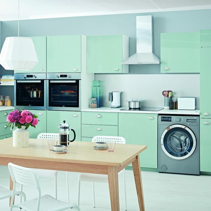 idėja, kaip įrengti modernią senovinę virtuvę, virtuvės fasado spalva žalia spalva pastelinės mėlynos sienos fone, medinis stalas ir metalinės kėdės, įdomus dizaino liustra