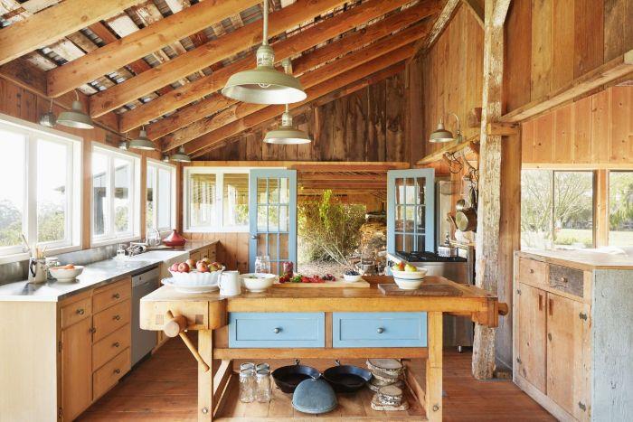 elegantna postavitev kuhinje v podeželskem slogu z izpostavljenimi tramovi in ​​lesenimi stenami osrednji otok miza lesena omara posoda, izpostavljena