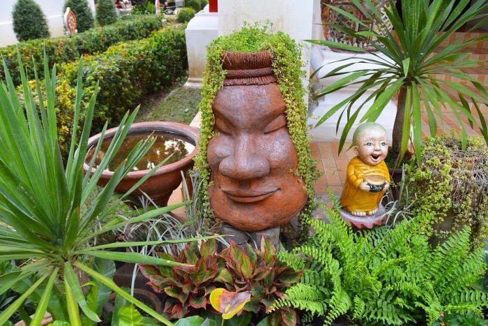 zen sodo išdėstymas, japoniškos statulos, vandens fontanas, buksmedis, krūmai ir palmė, egzotiška lauko deko idėja