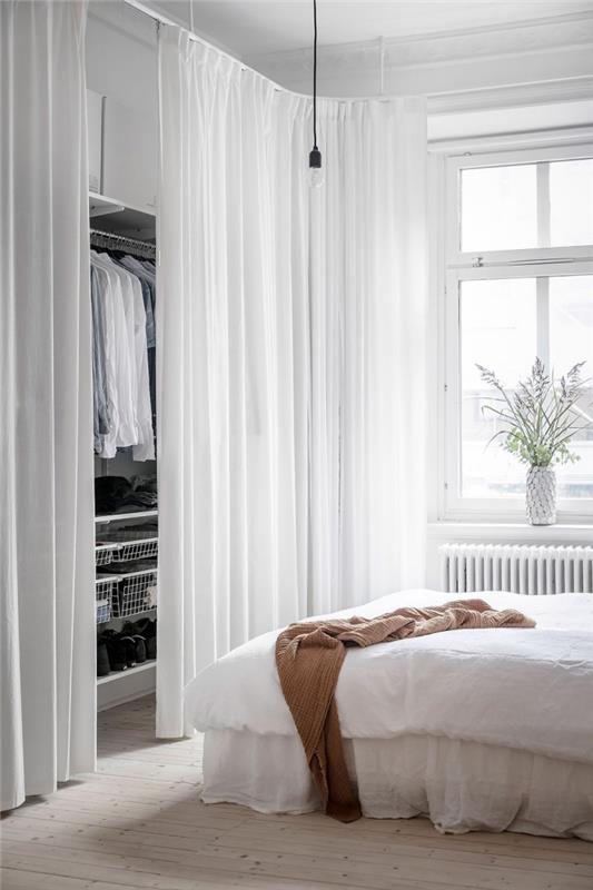 drabužinė su balta užuolaida, kuri įsilieja į balto miegamojo dekorą, drabužių laikymo sistema su drabužių bėgeliais, lentynomis ir krepšiais, kuriuos slepia užuolaidos