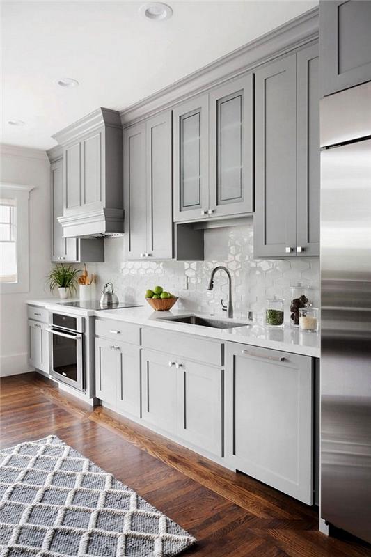parlak arkalık ve paslanmaz çeliğin mobilya rengiyle mükemmel bir şekilde birleştiği yerde, uzunlamasına döşenmiş gri ve beyaz bir mutfak