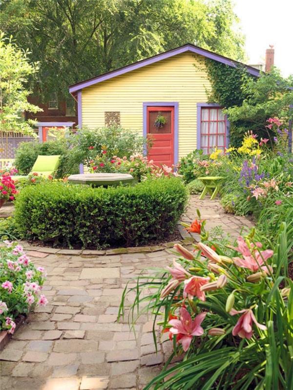 mažas sodas su akmeniniais takais, fontanas, apsuptas buksmedžio, gėlių lova, gulto kėdė nedidelio kaimo namo kieme