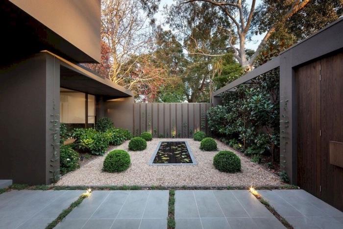 modernus sauso sodo išdėstymas, kvadratinė žvyro danga, buksmedžio žalia siena palei tvorą, mažas vandens tvenkinys, betoninių plokščių takas
