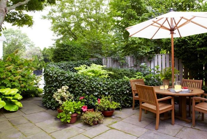 sodo išdėstymas su betoninių plokščių terasa, medinėmis kėdėmis ir stalu, skėčiu, buksmedžiu ir vazonėliais, medine tvora