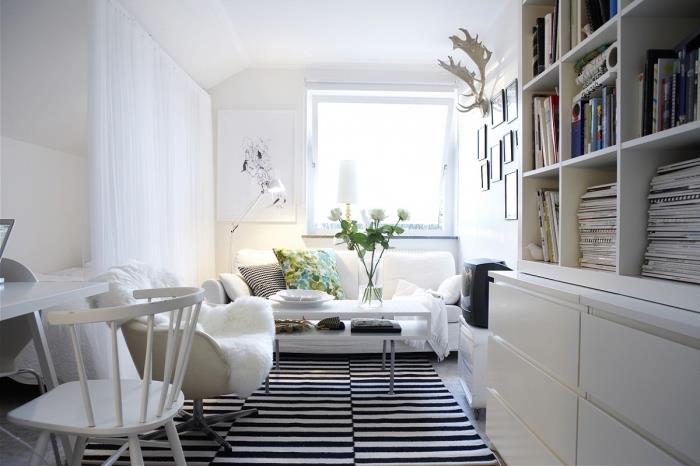 jauki atmosfera mažoje baltoje gyvenamojoje patalpoje, kurią maitina dryžuotas kilimas, skaitymo kampelis su jaukiu foteliu, papildytu baltu dirbtiniu kailiu