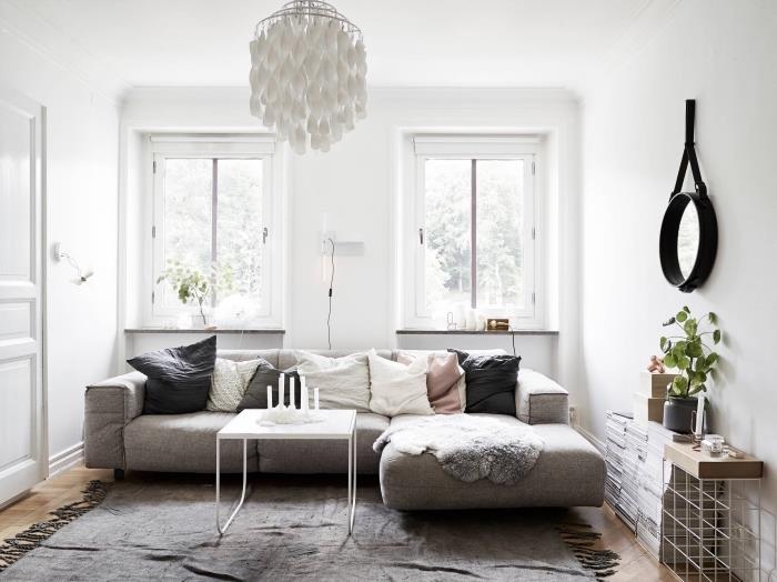 maža vienspalvė skandinaviška svetainė su jaukia pilka sofa, padengta dekoratyvinėmis lino pagalvėlėmis ir pakraščiu