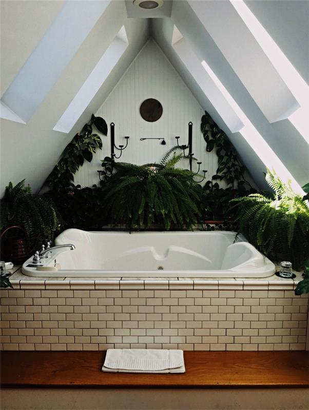 majhna kopalnica v mansardi, vgradna masažna kad pod pobočjem, obdana z zelenimi rastlinami za zen in naravno vzdušje