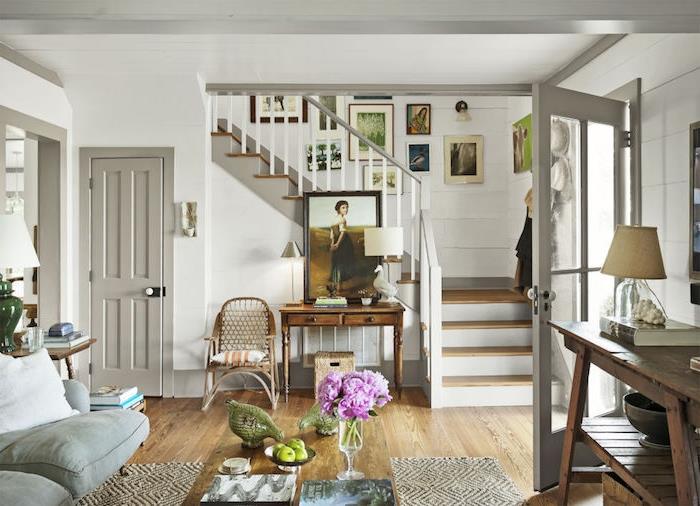 preprosta postavitev dnevne sobe v svetlo sivi beli in leseni barvi, leseni parket, okvir za stopnišče deco, vrata, kavč in sivo stopnišče, podeželski eleganten dekor