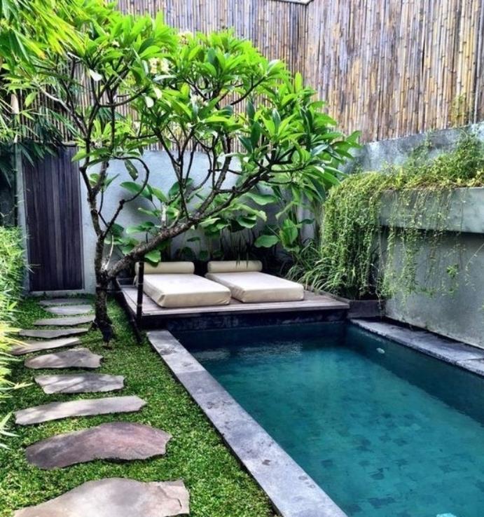 Japonų „zen ajrdin deco“ idėja su nedideliu vandens tvenkiniu, akmenukų taku ant žalios vejos, medžiu su žaliu vainiku, bambuku, salelių čiužinio poilsio zona