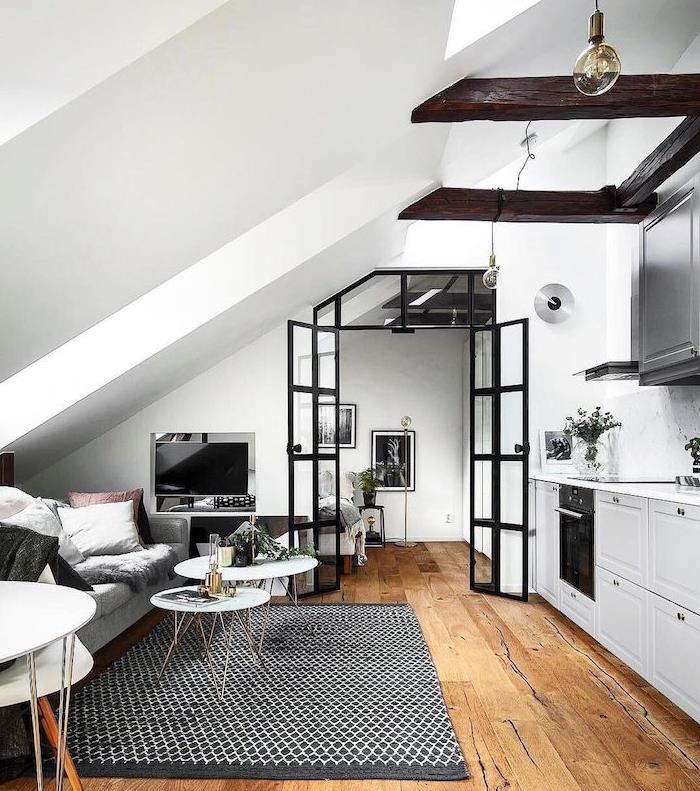 izpostavljeni tramovi v beli kuhinji, odprti do sive, rjave in bele dnevne sobe, črno-bela preproga, majhna postavitev studia v skandinavskem slogu
