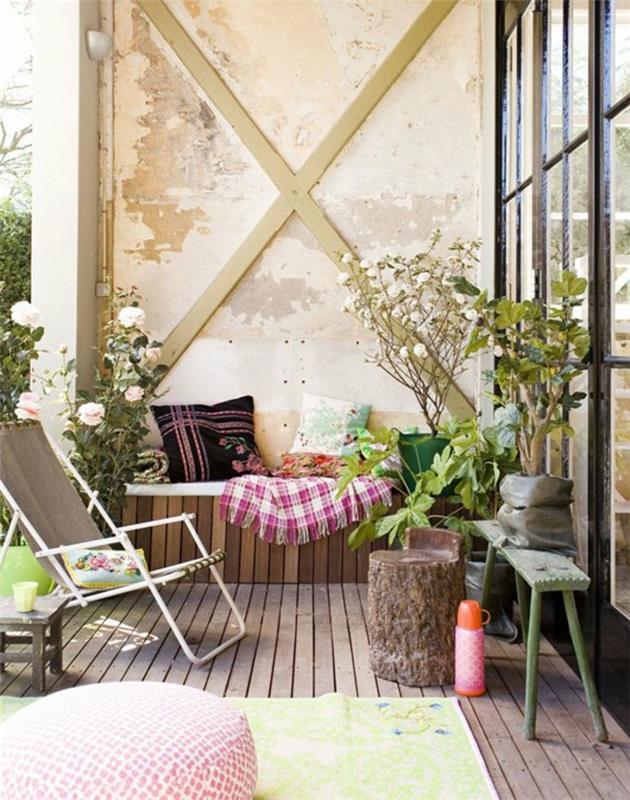 postavitev terase z majhno klopjo ob obrabljeni steni, zložljiv stol, kompozitna lesena talna obloga, svetlo zelena preproga, okrasne blazine, cvetoče rastline za balkon