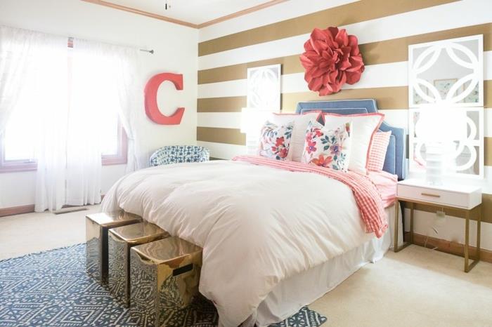 originalus suaugusiųjų miegamojo paveikslas, rožinė patalynė, rožinė galvūgalis, didelė gėlė ant sienos, baltos užuolaidos, mėlynas kilimas