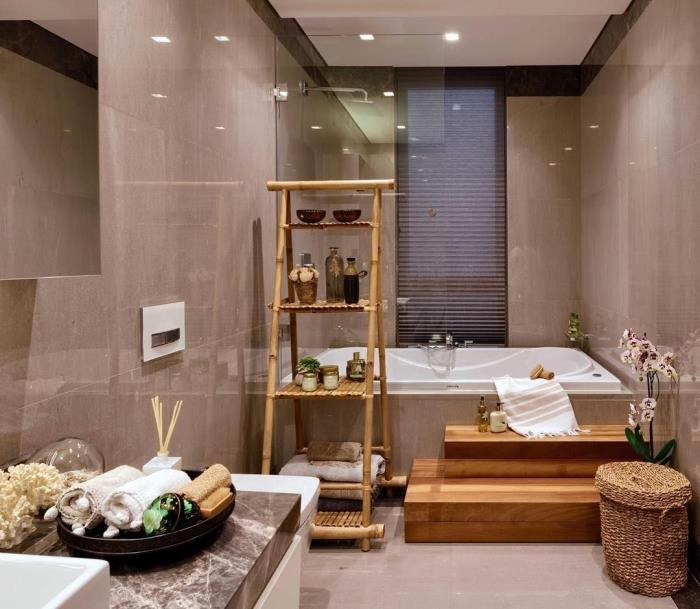 nedidelė vonia „Zen“ vonios kambaryje su šviesiai pilkomis sienomis, dekoruotomis medžio ir augalinio pluošto akcentais