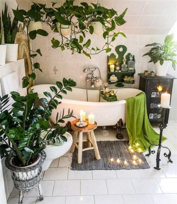 „Cocooning“ vonios kambario išdėstymas su keliais žaliais augalais vonios kambarys su plytelėmis išklotomis grindimis ir sienomis žvakės apšviečia girliandą aplink baltą vonią