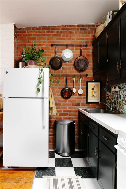 plytų siena, pakabinami indai, baltas šaldytuvas, juodos virtuvės spintelės, languotos plytelės, originalus virtuvės išdėstymas