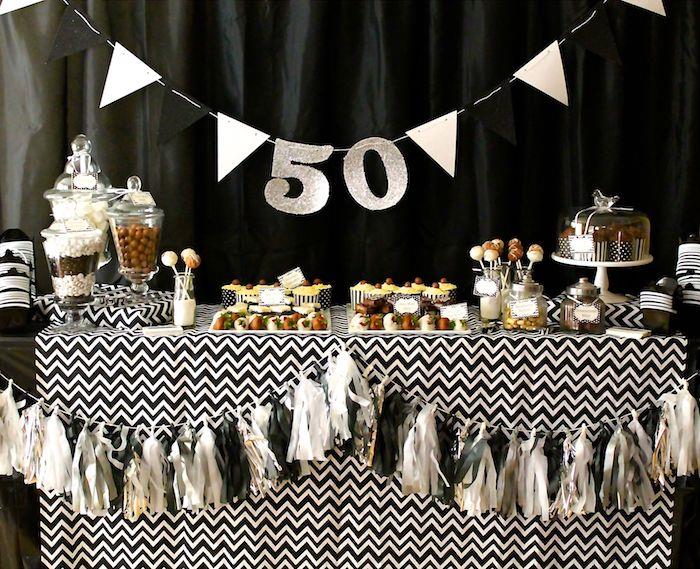 50 metų vimpelai ir laiškai girlianda, ševrono rašto staltiesės gimtadienio stalo dekoracijos, saldainių baro saldainiai, maži pyragaičiai, juodas fonas