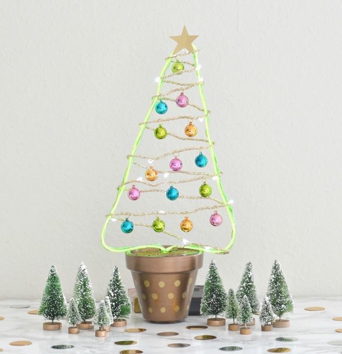 floresan yeşil telden oyulmuş ve led ışık çelenk ve küçük renkli Noel topları ile süslenmiş bir tencerede yapay bir Noel ağacı