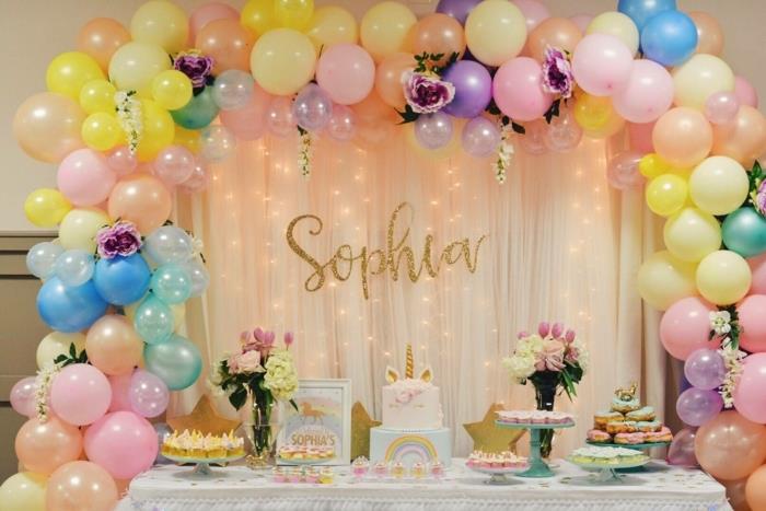 mažos mergaitės gimtadienis, virš stalo kabantys balionai, rožių puokštės, vienaragio pyragas, bandelės