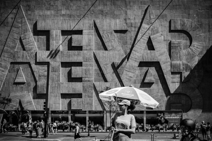 črno -bela fotografija ženske na ulici, ki stoji pred fasado stavbe v Braziliji