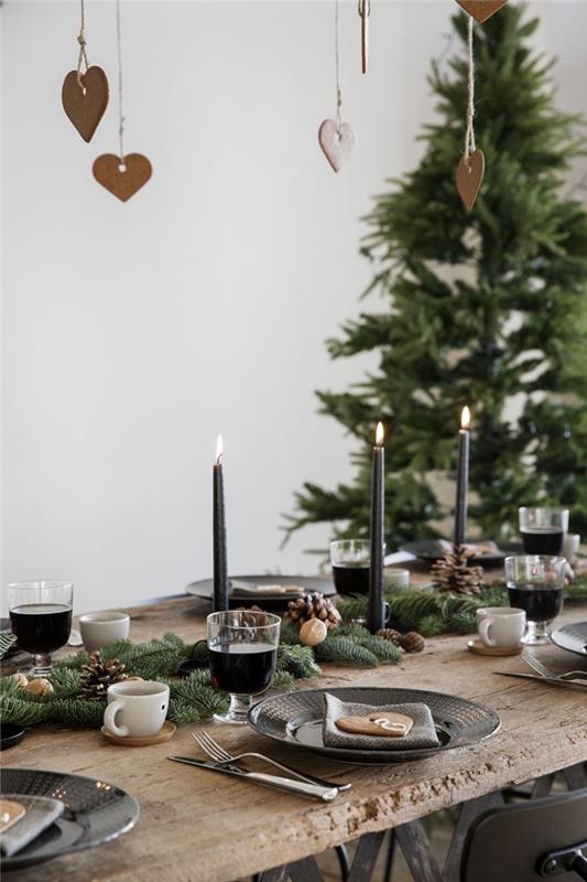 pavyzdys, kaip modernaus stiliaus stalą papuošti mediniais daiktais ir matine juoda spalva, Kalėdų centrą eglės šakomis ir žvakėmis