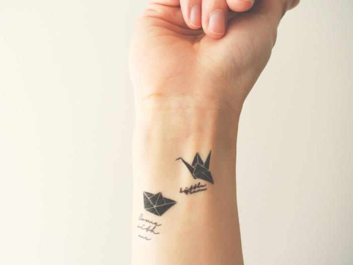 prikupna minimalistična tetovaža na zapestju, sestavljena iz majhnega origami žerjava in papirnatega čolna, povezanega s kaligrafskimi besedami