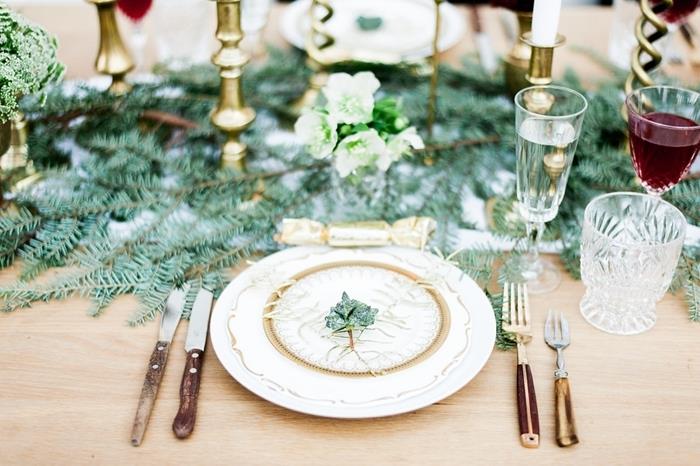bela in zlata plošča zelene veje okraski za božično mizo kozarci leseni pokrovi zlati svečniki lesena miza