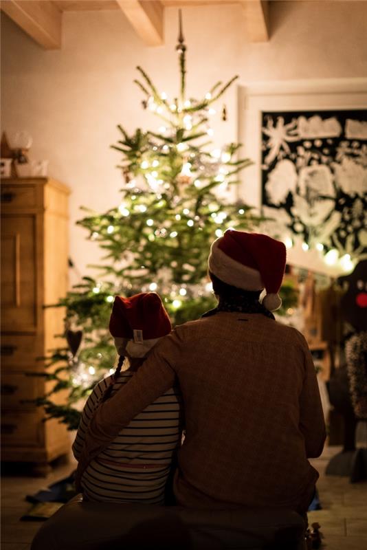 Linksmų Kalėdų vaizdas su vaiku ir jo tėvu priešais natūralų medį gyvenamajame kambaryje, šeimos Kalėdų nuotraukos idėja