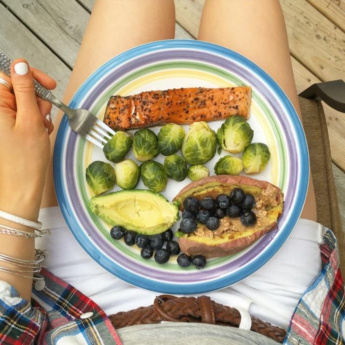 ženska s krožnikom, polnim ribjih filetov, avokada in robide, uravnotežena prehrana, bele jeans hlače