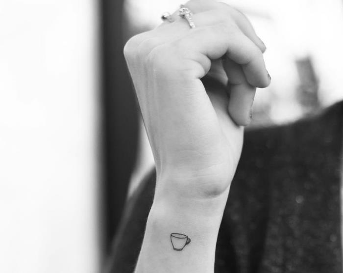belo -črna fotografija, ki ponazarja minimalistično oblikovano žensko tetovažo na zapestju z majhno risbo s črnilom z vzorcem kave